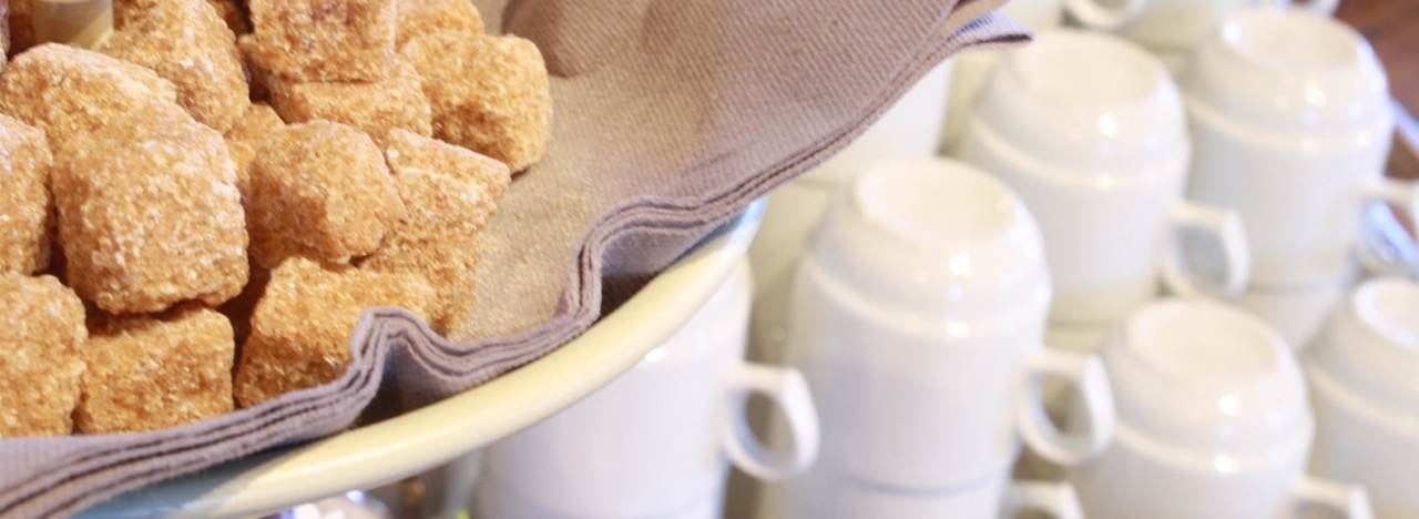 Sukkerbiter i skål og stabler av hvite kaffekopper