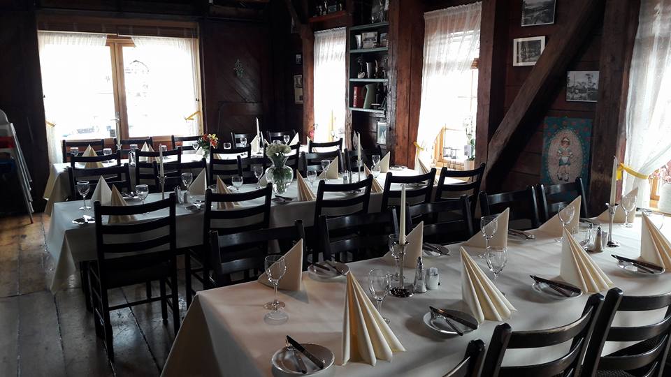 Salen dekket til selskap, med hvite duker, brettede servietter og tømmervegger